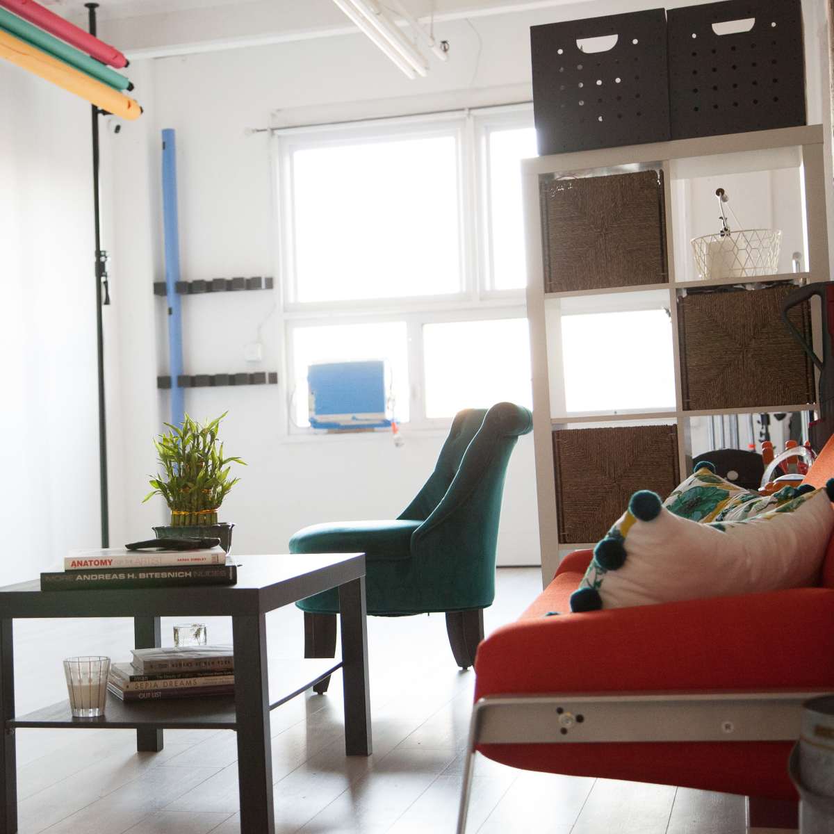 A bright room features a red sofa, a green chair, a coffee table, and various storage bins along the walls.