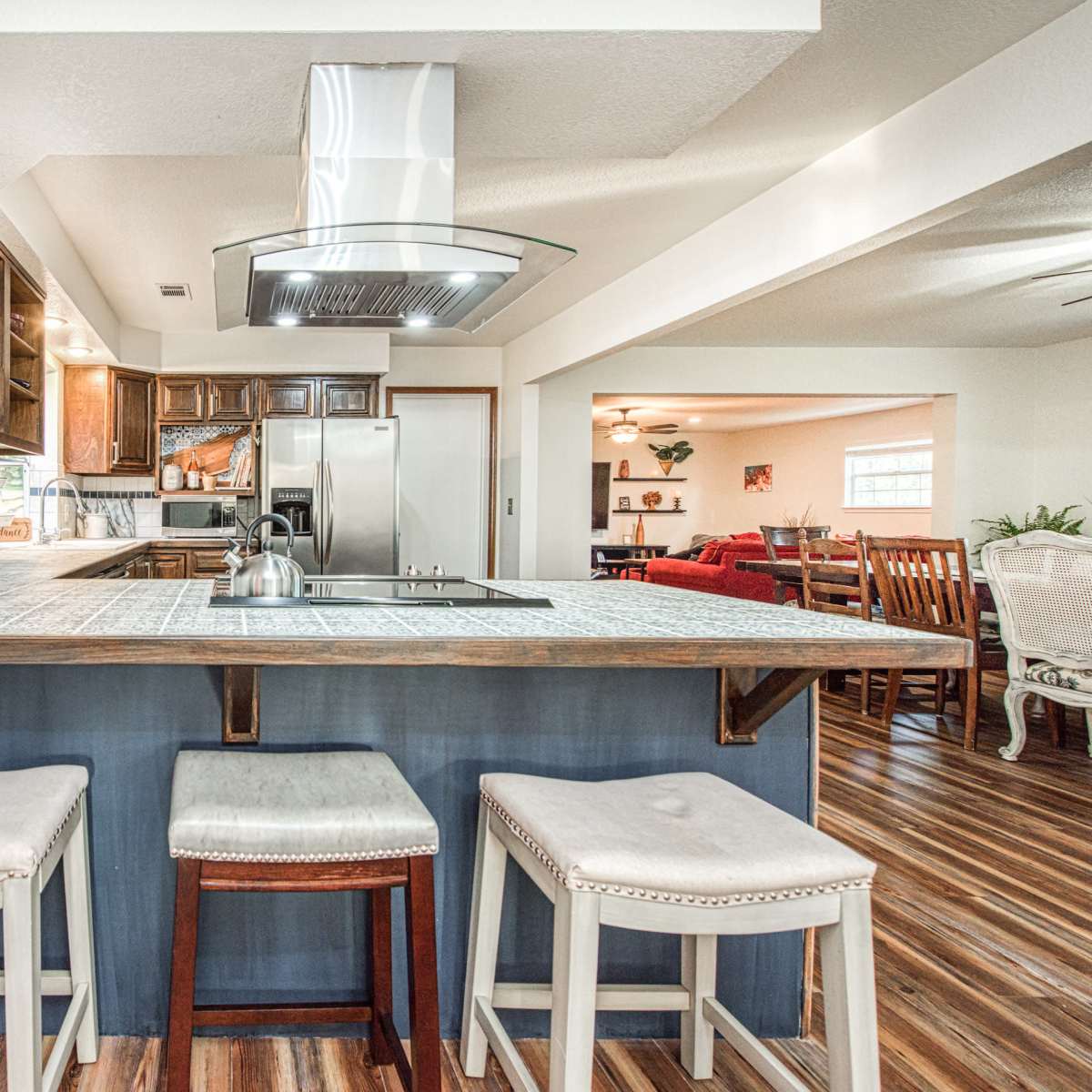 A modern kitchen with a center island, featuring three bar stools and stainless steel appliances in the background.
