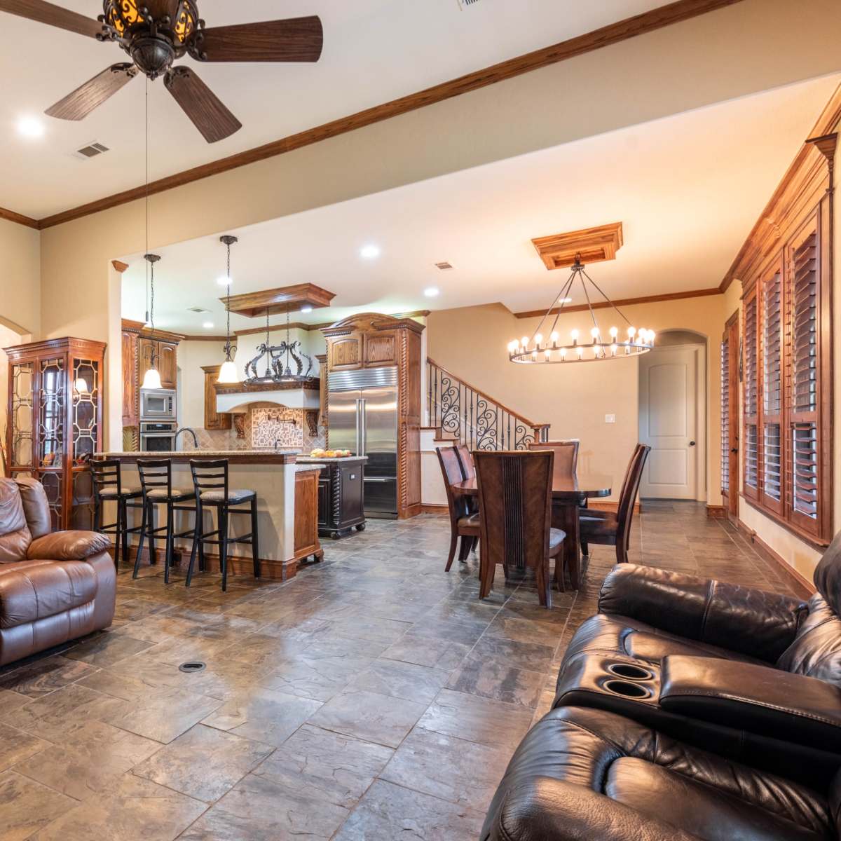 A spacious living area featuring leather sofas, a kitchen with dark wood cabinetry, and a dining area illuminated by a chandelier.