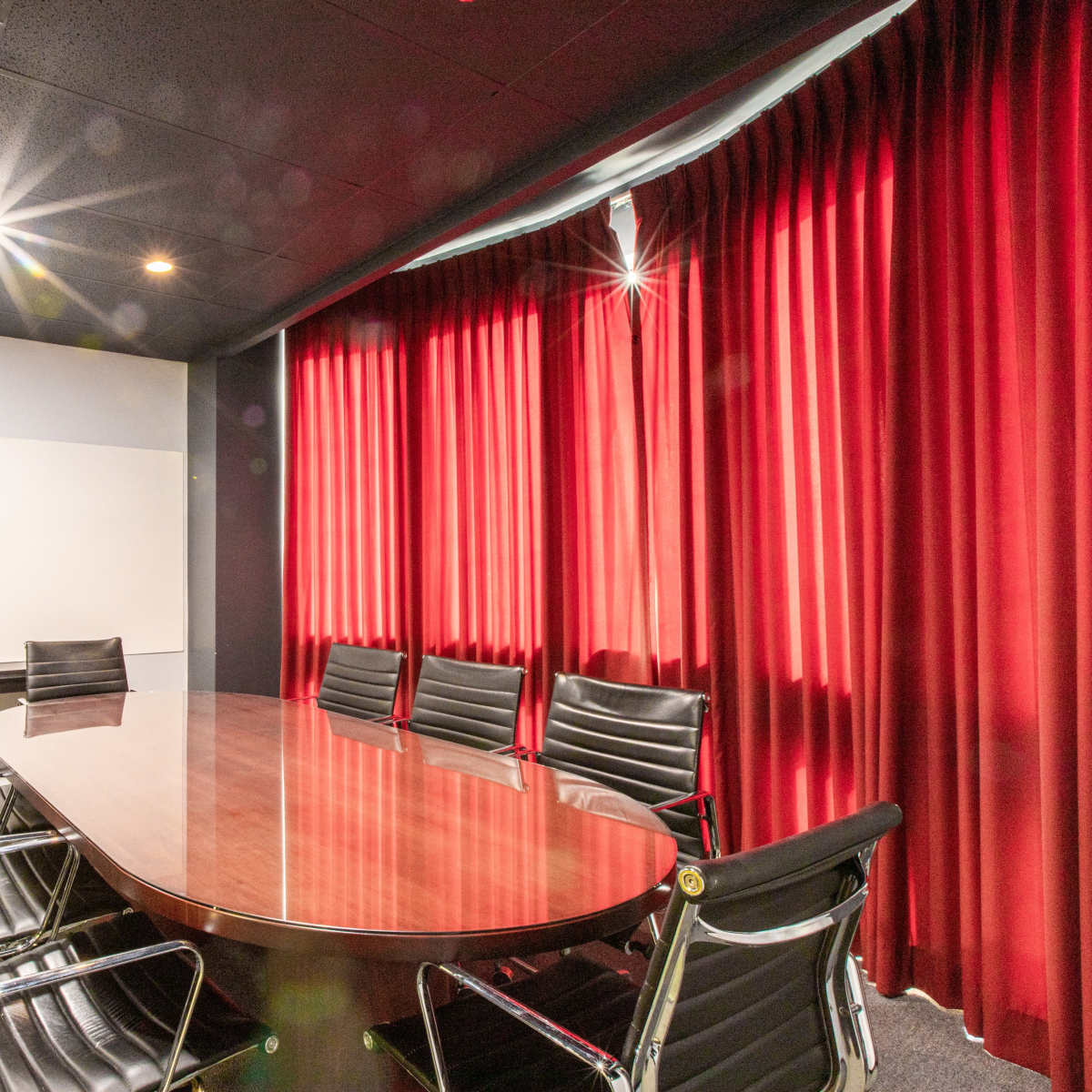 A conference room features a round wooden table surrounded by black leather chairs and red curtains.