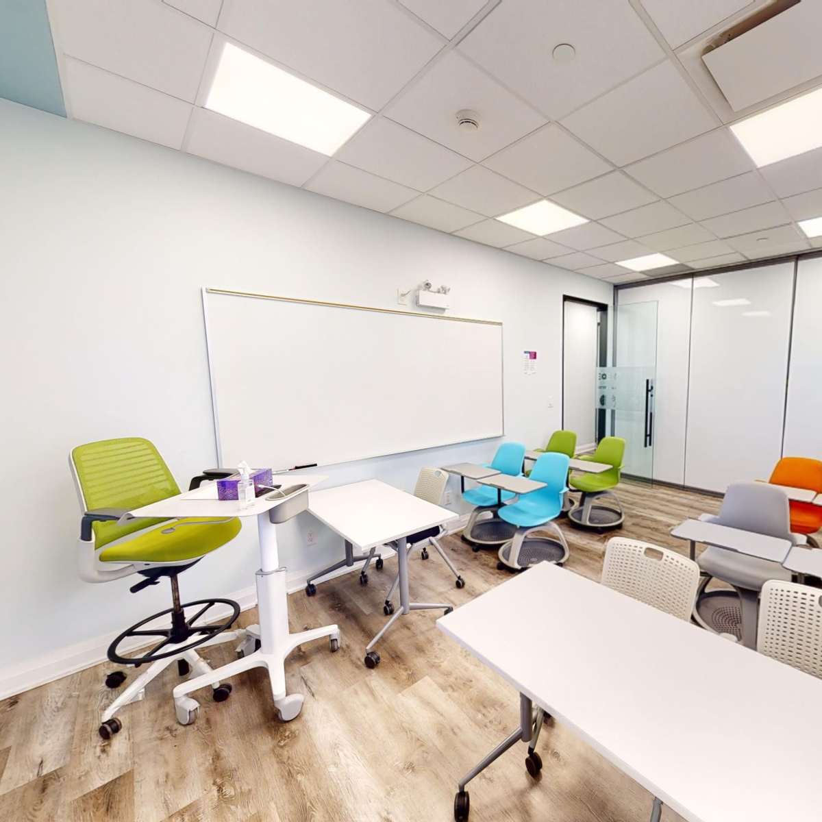A modern classroom equipped with movable furniture, a whiteboard, and large windows offering natural light.