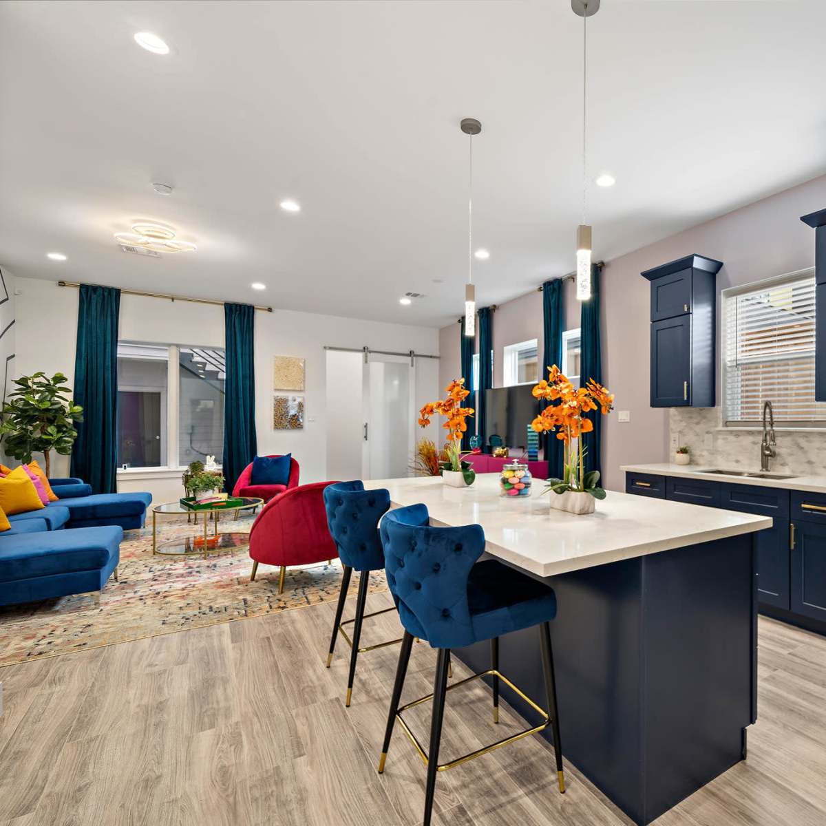 A modern kitchen and living area with navy blue cabinetry, a bright island with bar stools, and colorful furnishings.