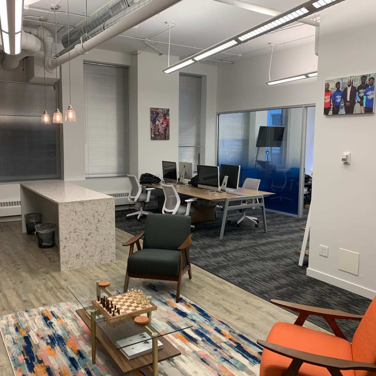 A modern office space featuring a seating area with chairs, a communal table, and multiple workstations in a well-lit environment.