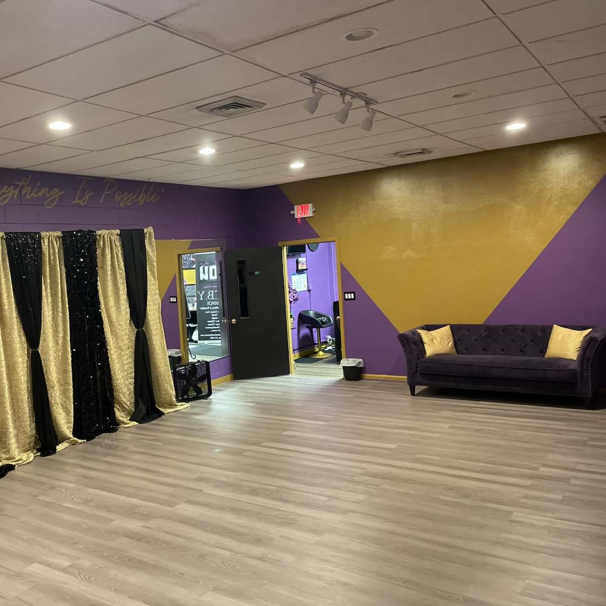 A dance studio interior with purple and gold walls, a black and gold curtain backdrop, and a dark purple sofa.