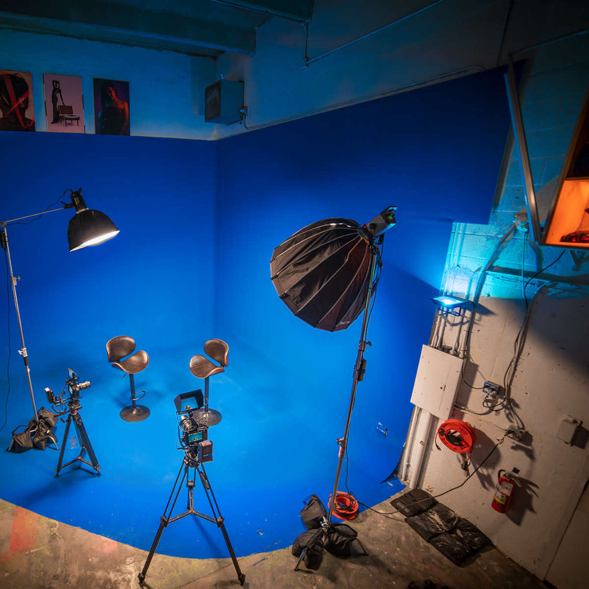 A photo studio with a blue backdrop, two empty chairs, and various lighting equipment set up for a shoot.