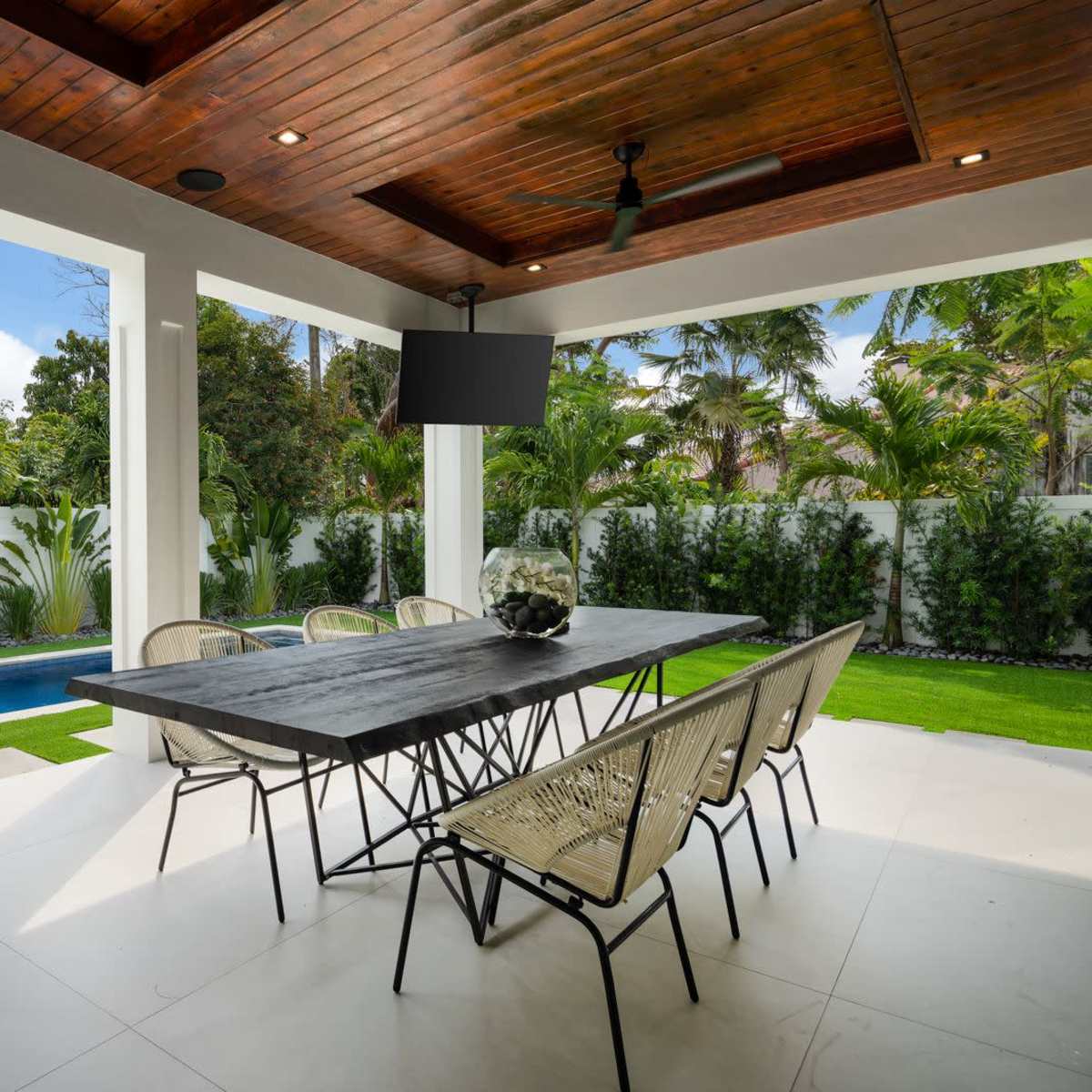 An outdoor dining area with a large table and chairs, overlooking a small pool surrounded by greenery.