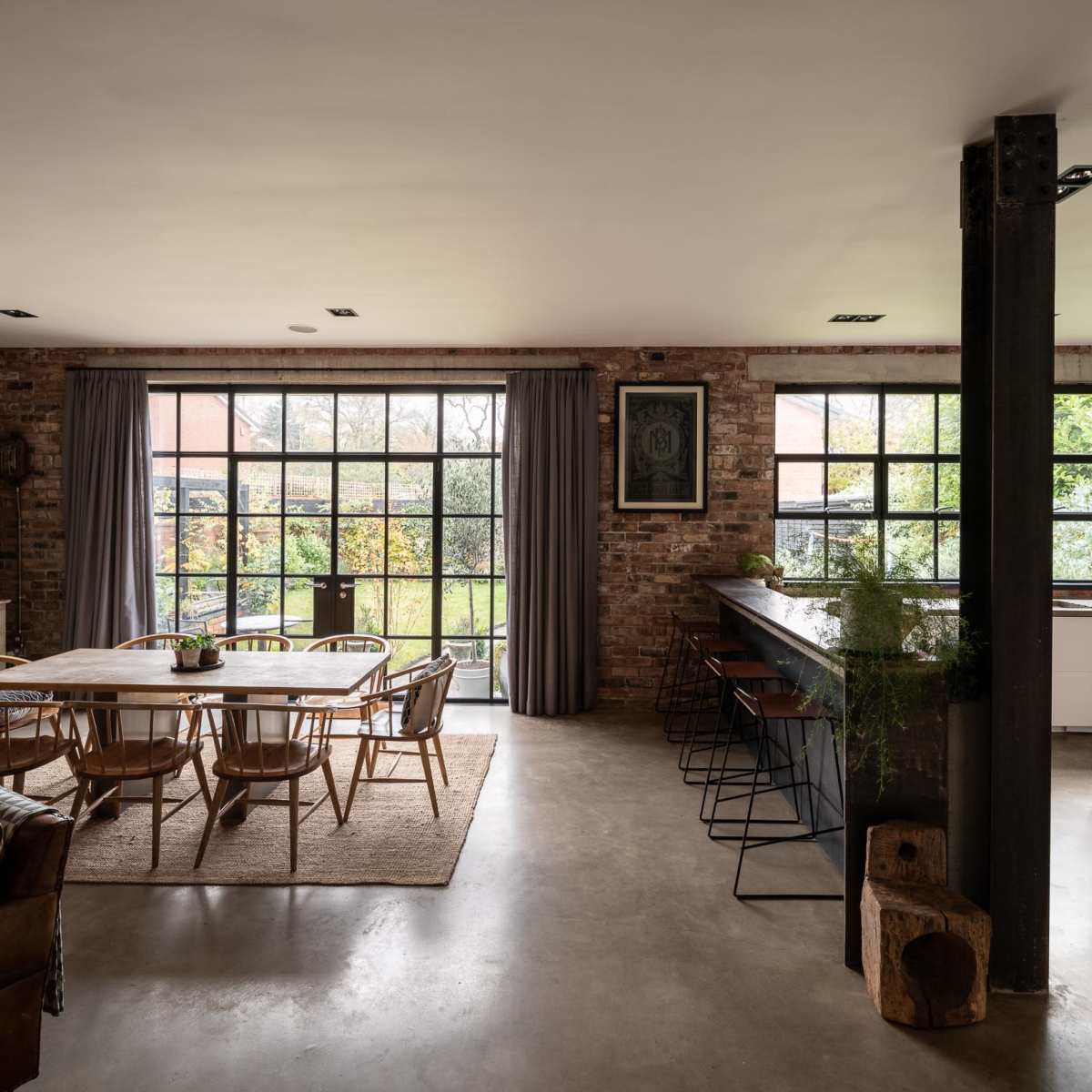 A spacious, modern kitchen and dining area with large windows and a mix of rustic elements and contemporary furniture.