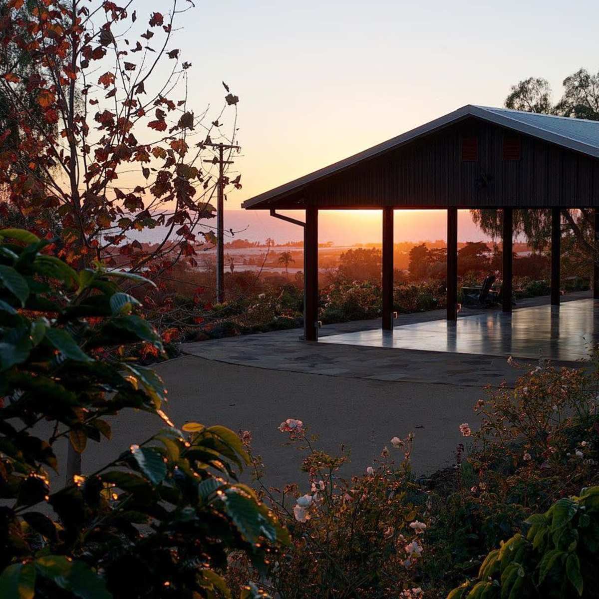 A pavilion with a slanted roof stands beside a pathway, framed by colorful foliage as the sun sets in the background.