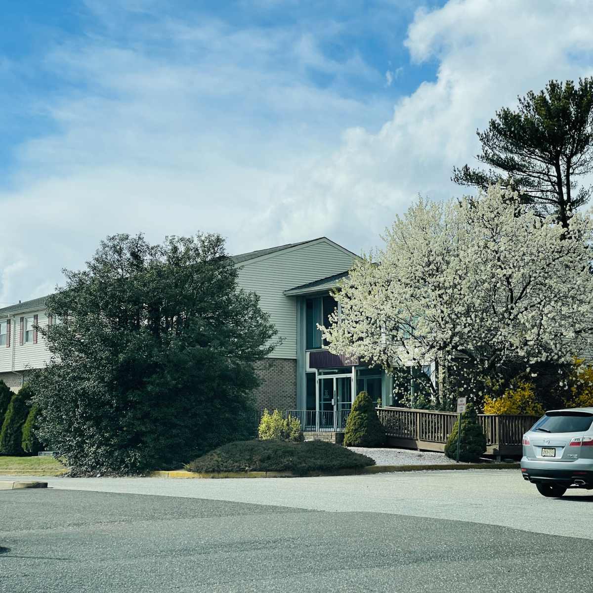 A building with a landscaped exterior featuring flowering trees and shrubbery is seen under a partly cloudy sky.