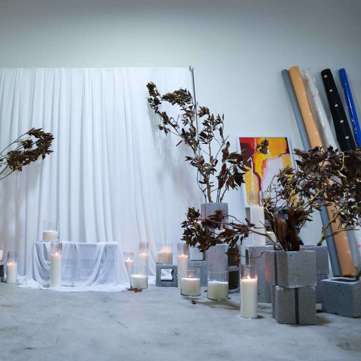 A simple display features a white backdrop, a covered table, and candles arranged among decorative branches and concrete blocks.