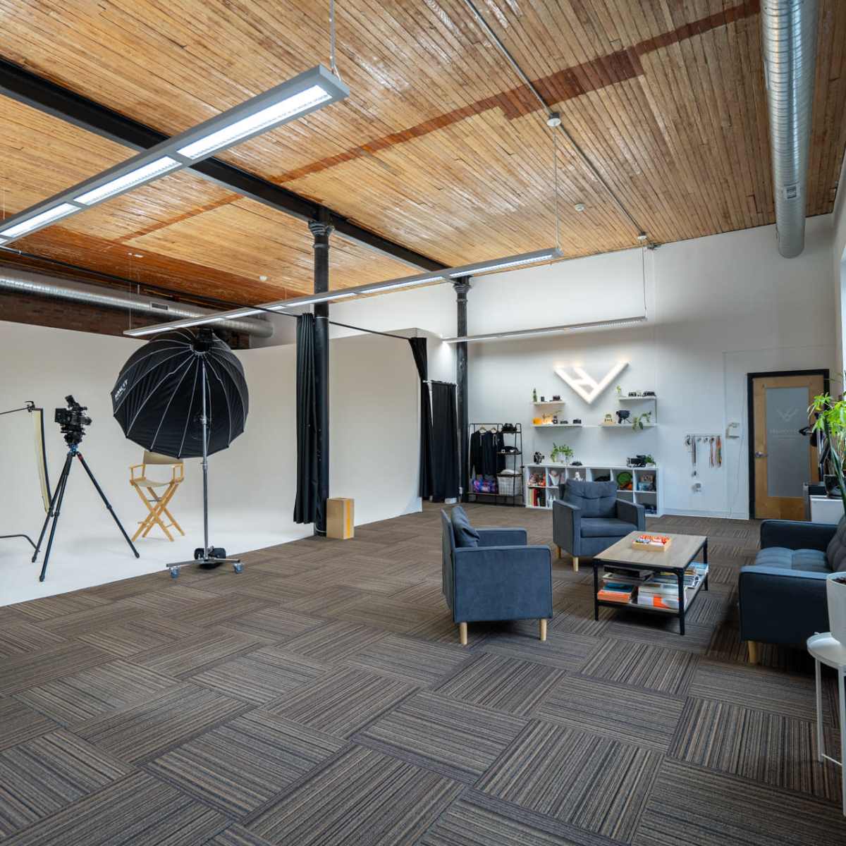 A spacious studio with a white backdrop, photography equipment, and a seating area furnished with gray sofas and decorative plants.