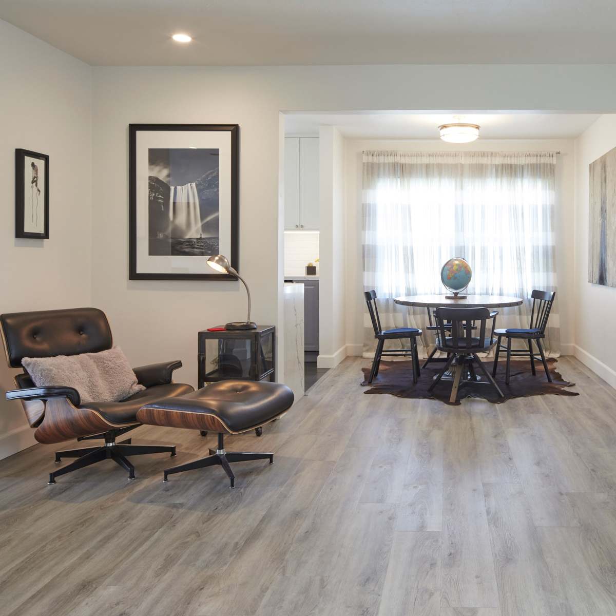A modern living space featuring a black leather chair, a circular dining table with chairs, and a white brick fireplace.