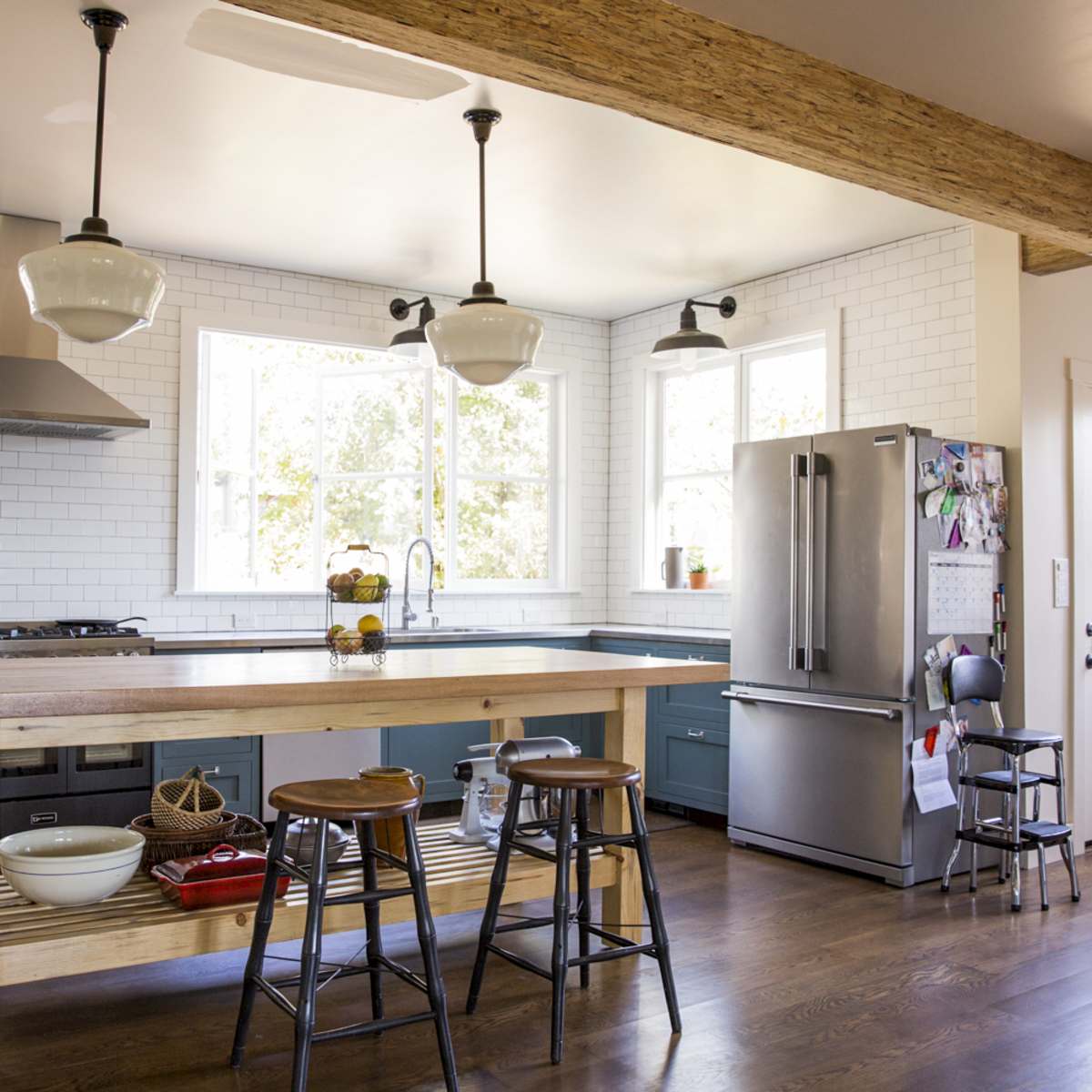 A modern kitchen with blue cabinetry, a large wooden island with stools, and multiple windows allowing natural light to enter.