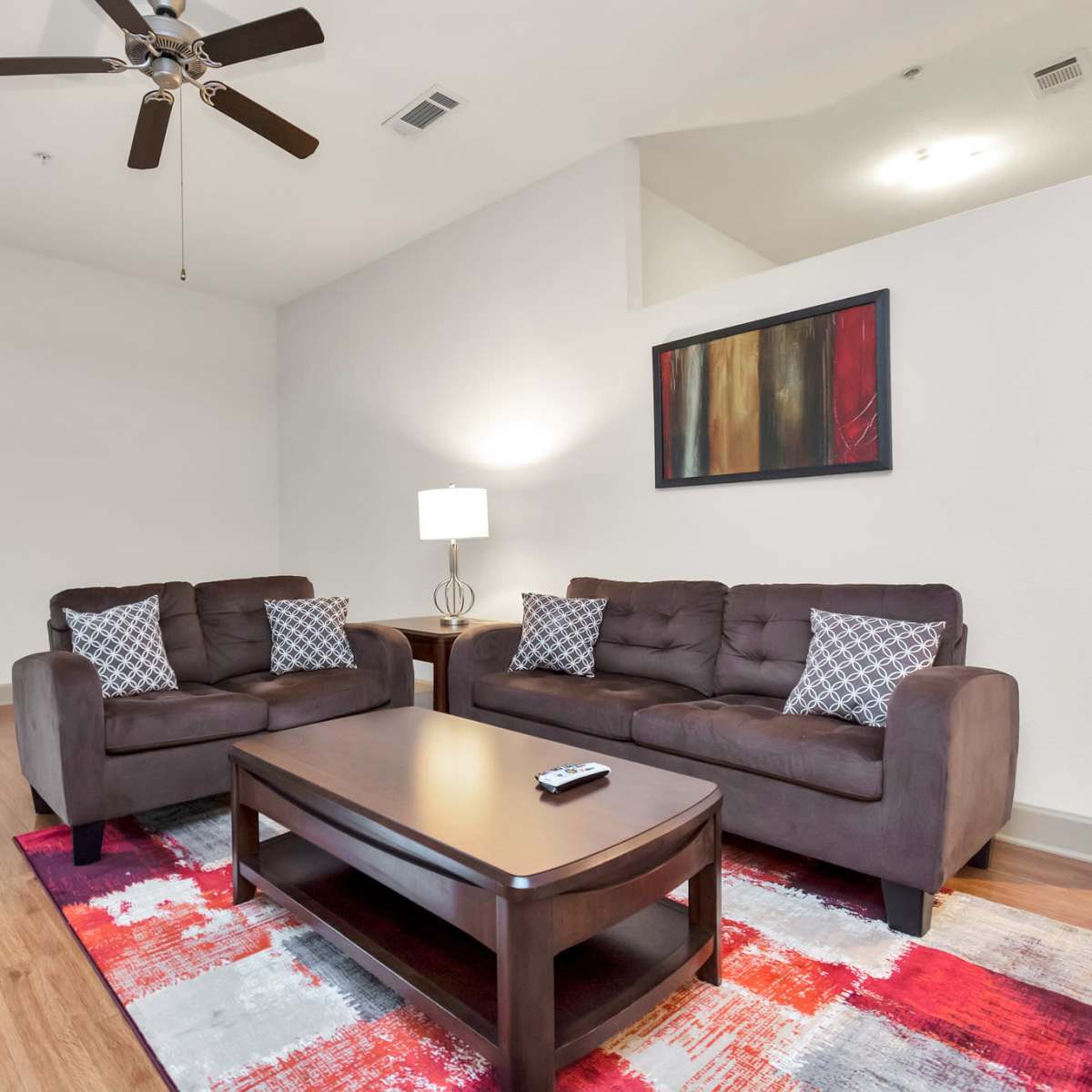A modern living room featuring two brown sofas, a coffee table, a lamp, and a colorful area rug.