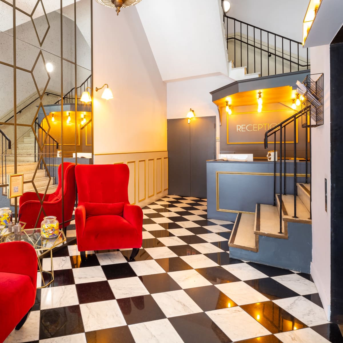 A stylish hotel lobby with a checkerboard floor, red velvet chairs, a reception desk, and mirrors creating an elegant atmosphere.