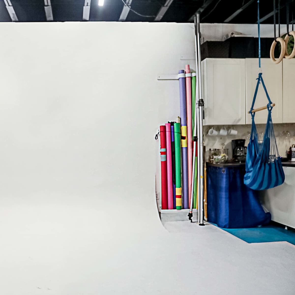 A photography studio with a white backdrop and various colorful rolled backdrops stored along one side.