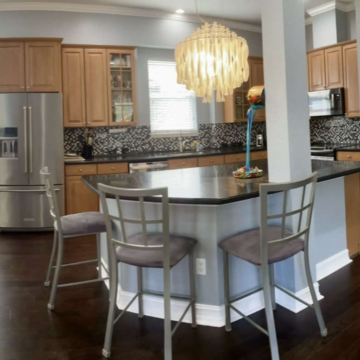 A modern kitchen with wooden cabinets, stainless steel appliances, and a breakfast bar with stools, adjacent to a dining area featuring a table and chairs.