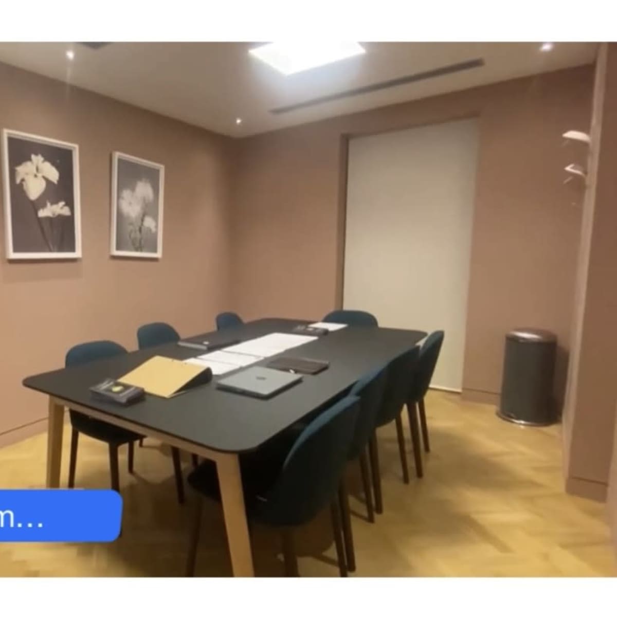 A private meeting room features a large table surrounded by chairs, with framed floral artwork on the walls.