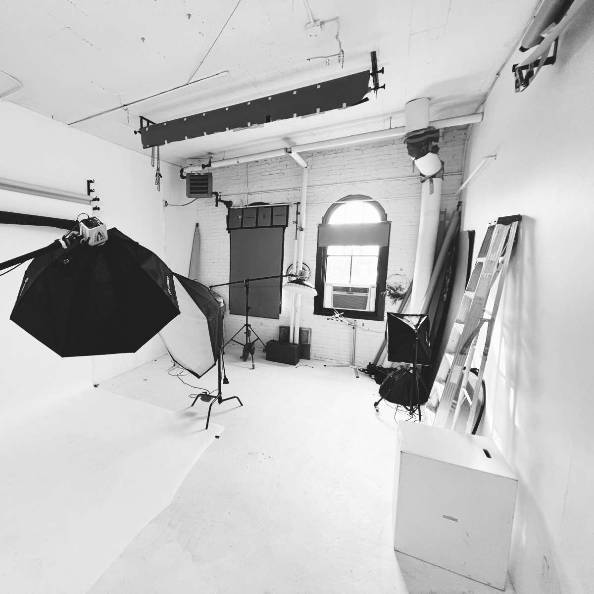 A photography studio with various lighting equipment and a large white backdrop.