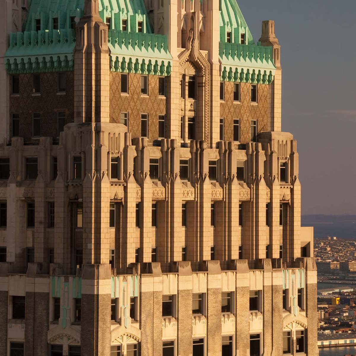 The upper portion of a historic skyscraper featuring a green copper roof and intricate architectural details.