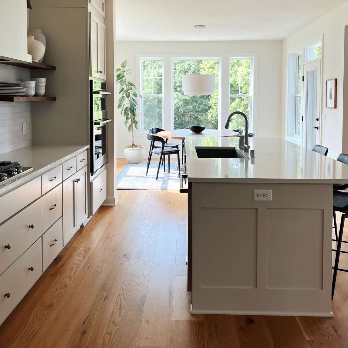 A modern kitchen features a central island, built-in appliances, and large windows that allow natural light to fill the space.