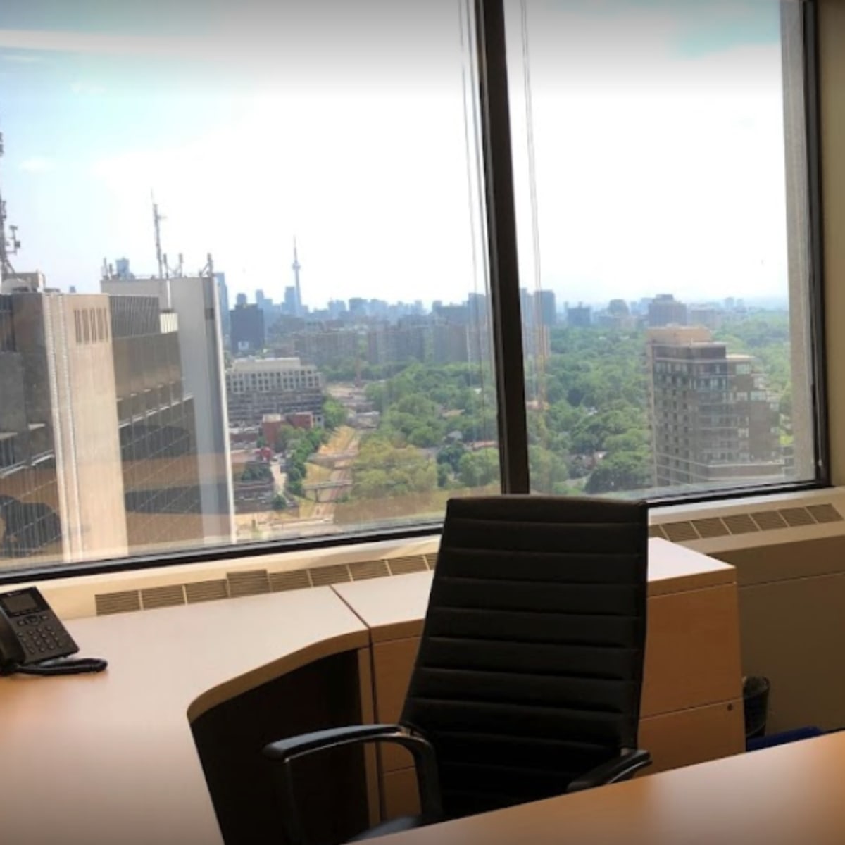 An office interior featuring a desk and chair, with large windows offering a view of a city skyline.