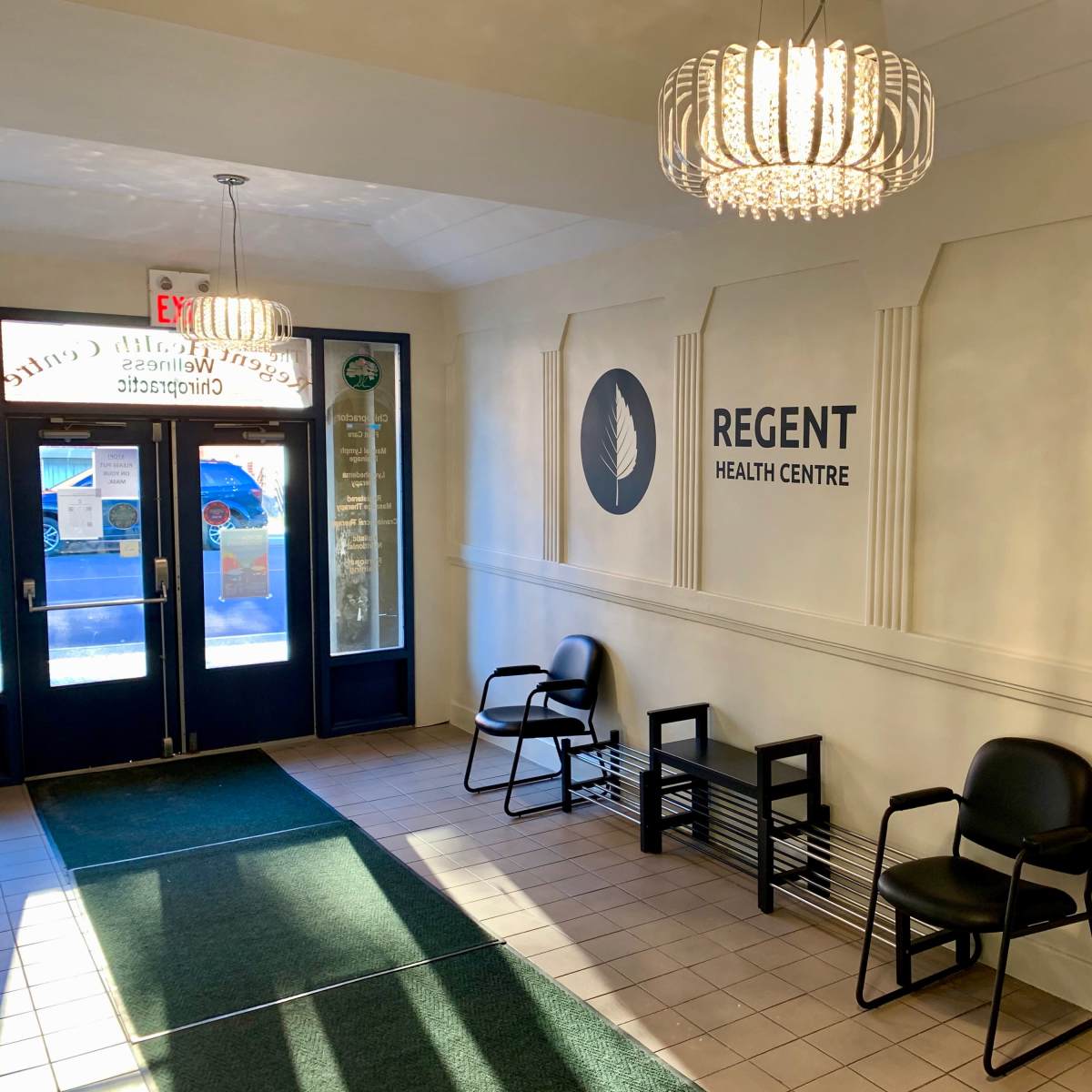 The entrance of Regent Health Centre features chairs against a wall with the center's logo and two modern light fixtures above.