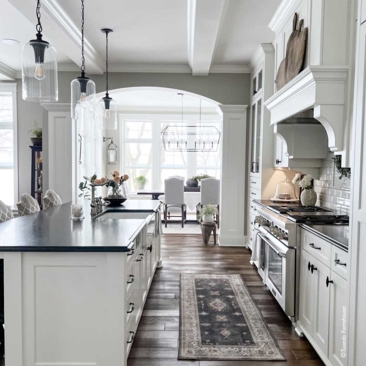 A modern kitchen with a central island, pendant lighting, and a dining area visible through an archway.