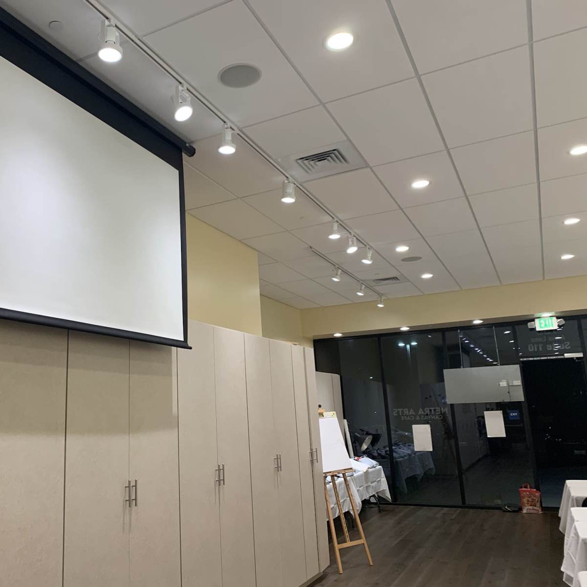 A conference room featuring a large projection screen mounted on a wall, with beige cabinetry and bright overhead lighting.