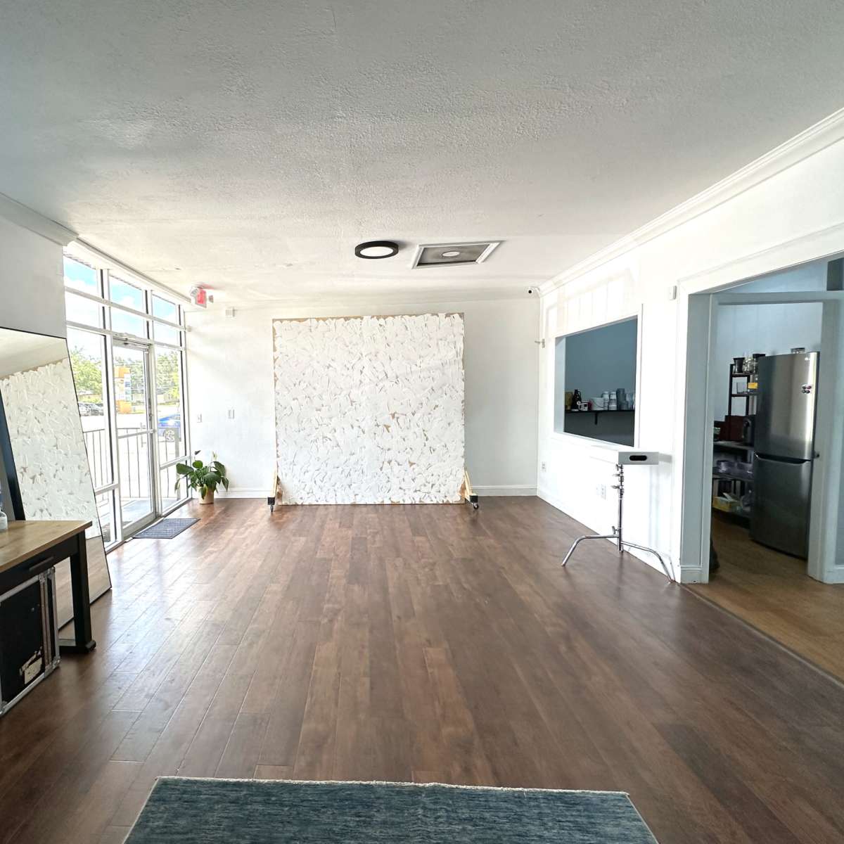 A spacious, well-lit room featuring a wooden floor, a large mirror, and a textured white wall at the far end.