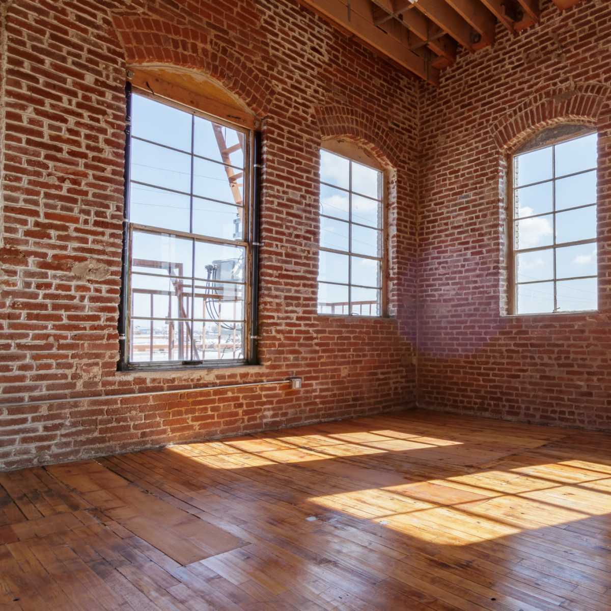 The room features exposed brick walls, large windows, and a polished wooden floor.
