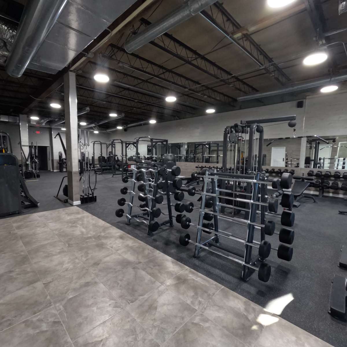 An empty gym interior with various exercise equipment, including weightlifting machines and dumbbells, arranged in an open layout.