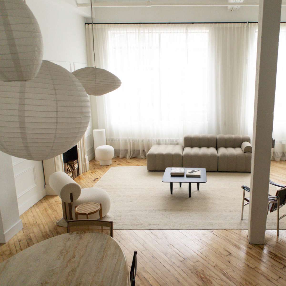 A spacious, modern living area features a minimalist design with large windows, a light-colored sofa, a round table, and various decorative elements.