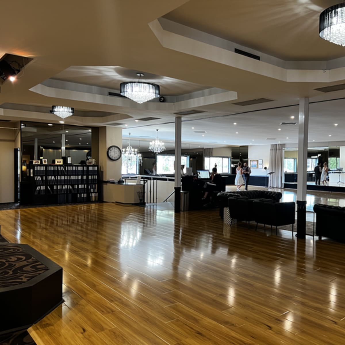 The spacious interior features a polished wooden floor, modern chandeliers, and seating areas with dark furnishings.