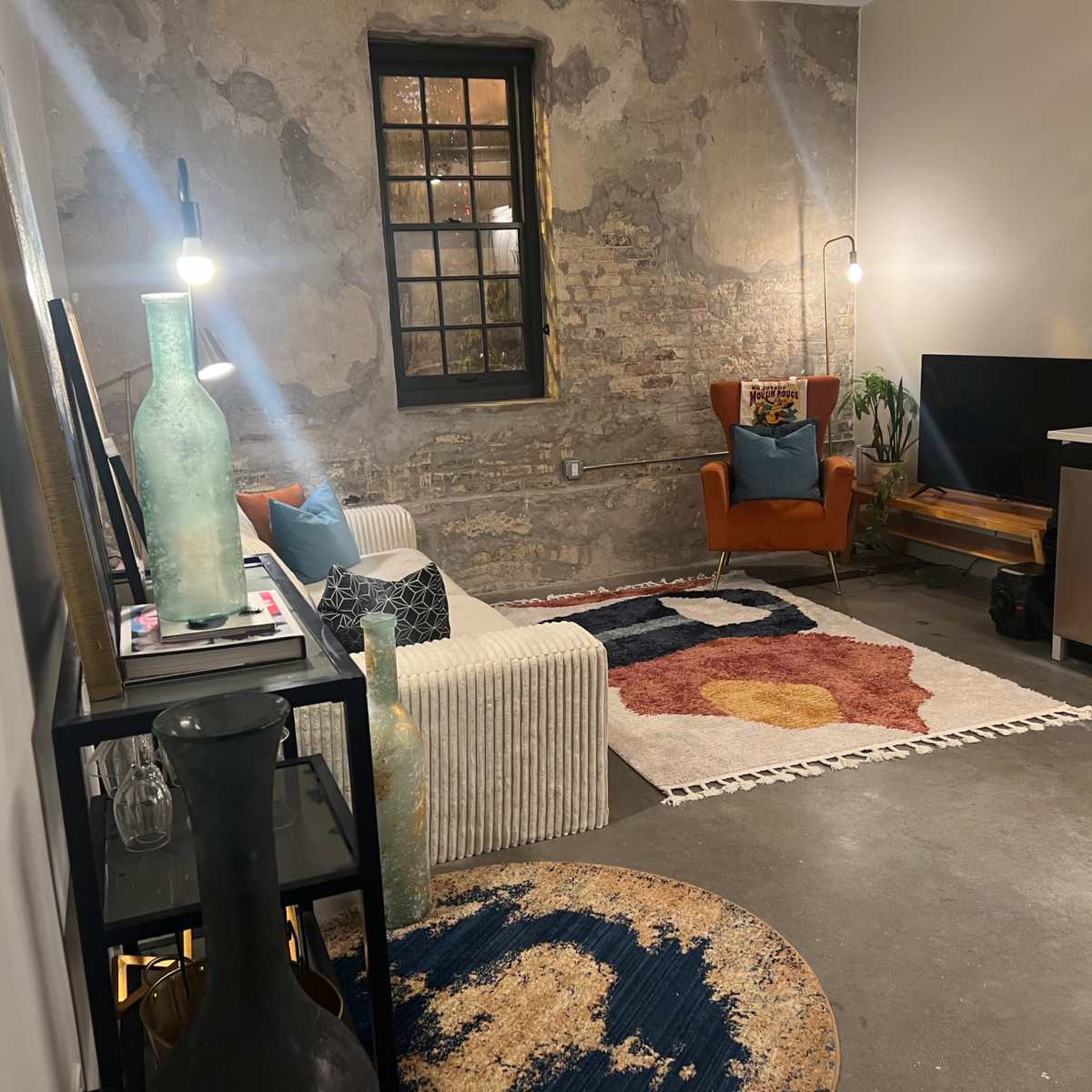 A modern living room with a textured stone wall, a white sofa, a colorful area rug, a television, and a small dining area.