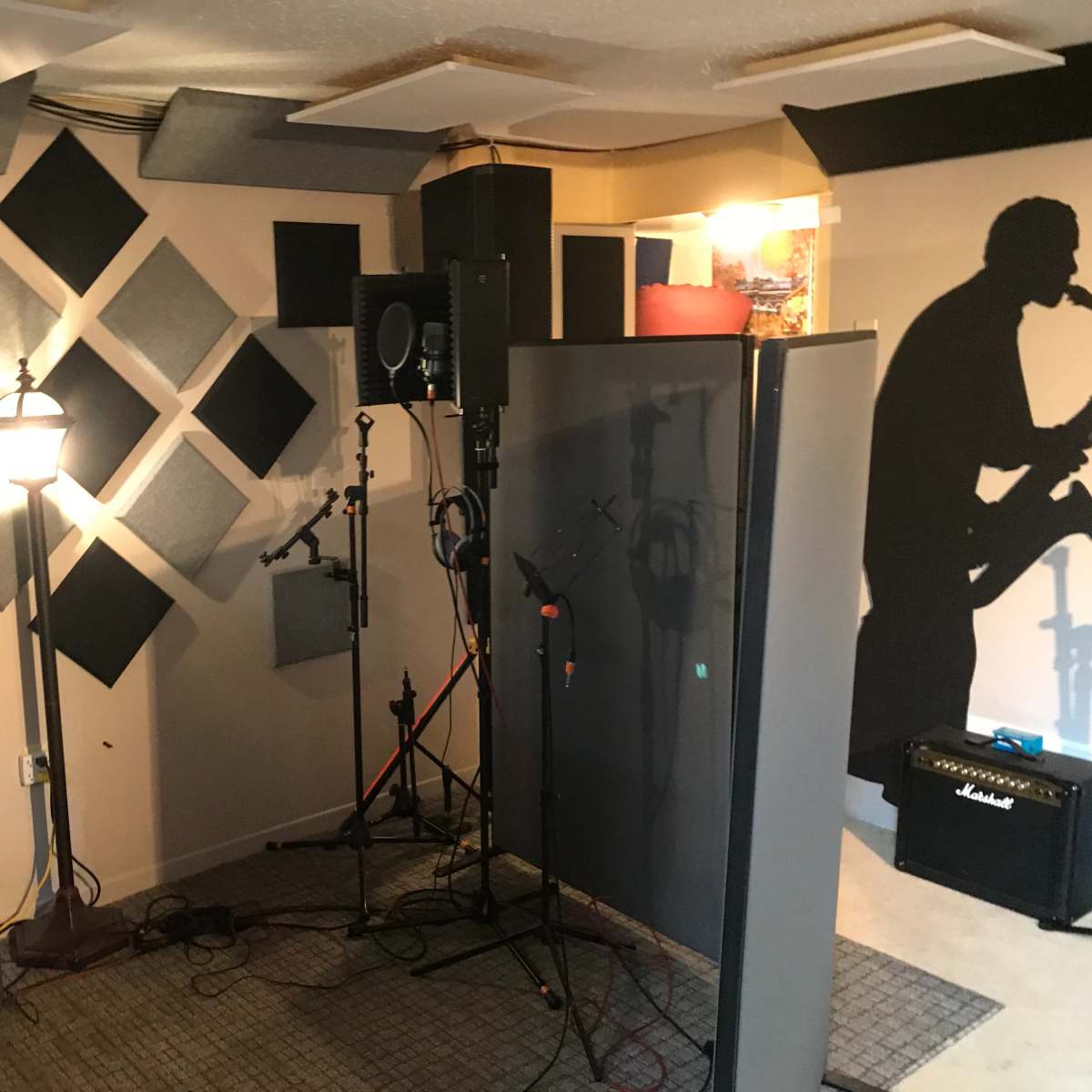 A soundproof recording studio with acoustic panels on the walls and a microphone setup, including a guitar amplifier in the corner.