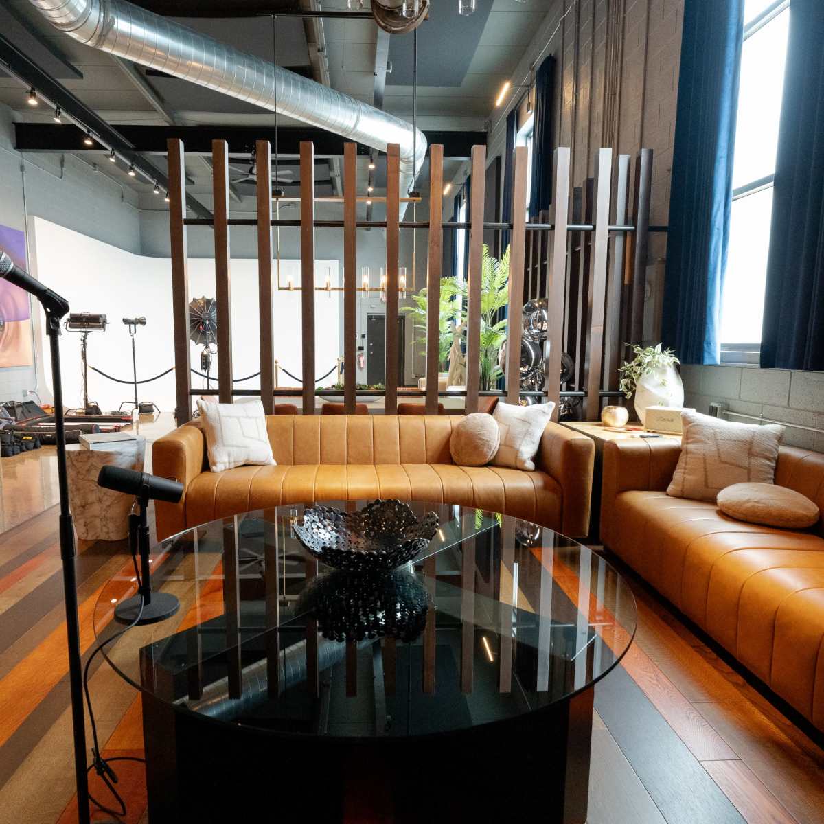 A modern lounge area featuring two brown leather sofas, a glass coffee table, and large windows with dark curtains.