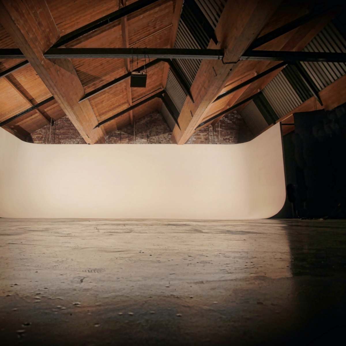 A spacious, empty studio with a curved backdrop and wooden beams overhead.