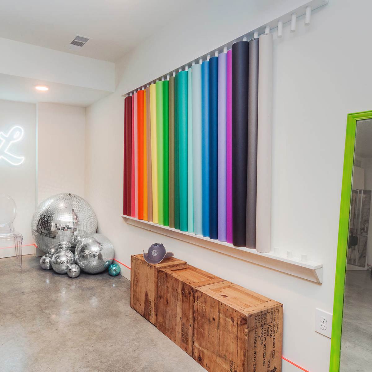 A brightly colored interior space featuring a yellow sofa, a wall with various colored vertical stripes, and shiny disco balls arranged near a wooden crate.