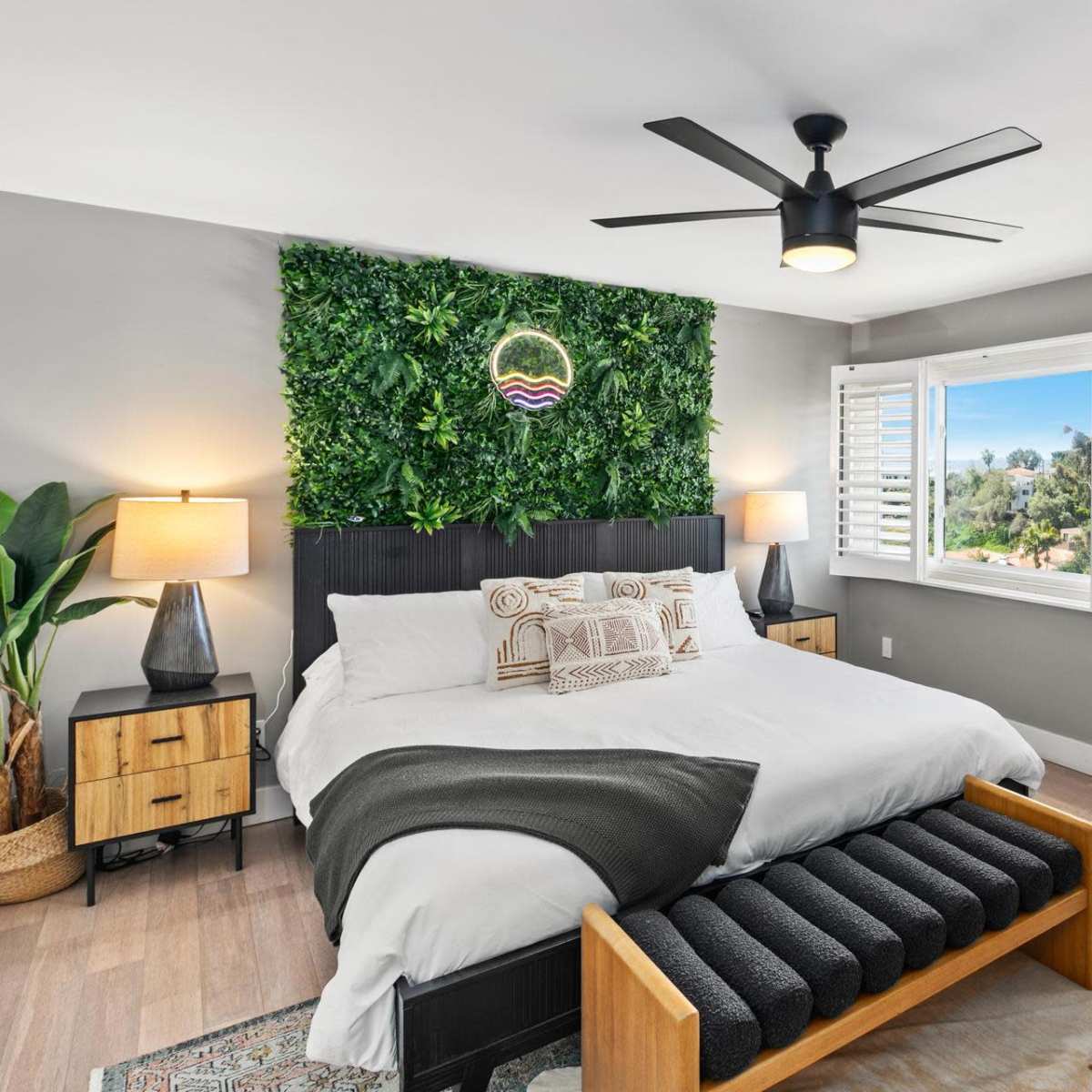 The bedroom features a large bed with a green wall decoration, large windows with shutters, and a mirror beside a standing lamp.