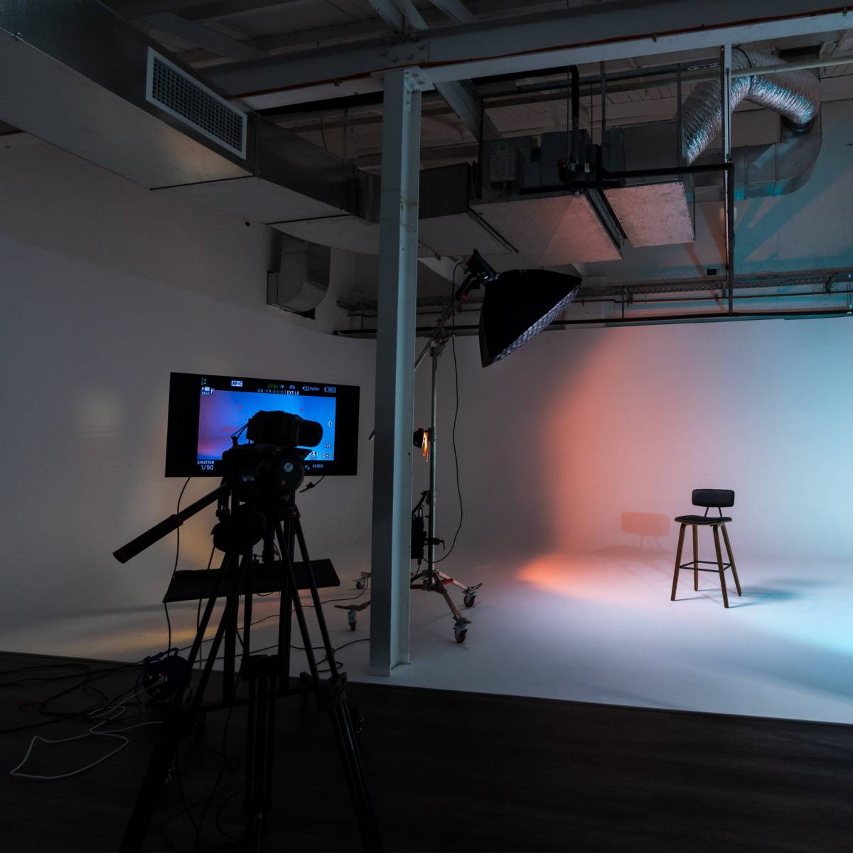 A photography studio is set up with a gradient background, a stool, and multiple light sources, alongside a camera on a tripod.
