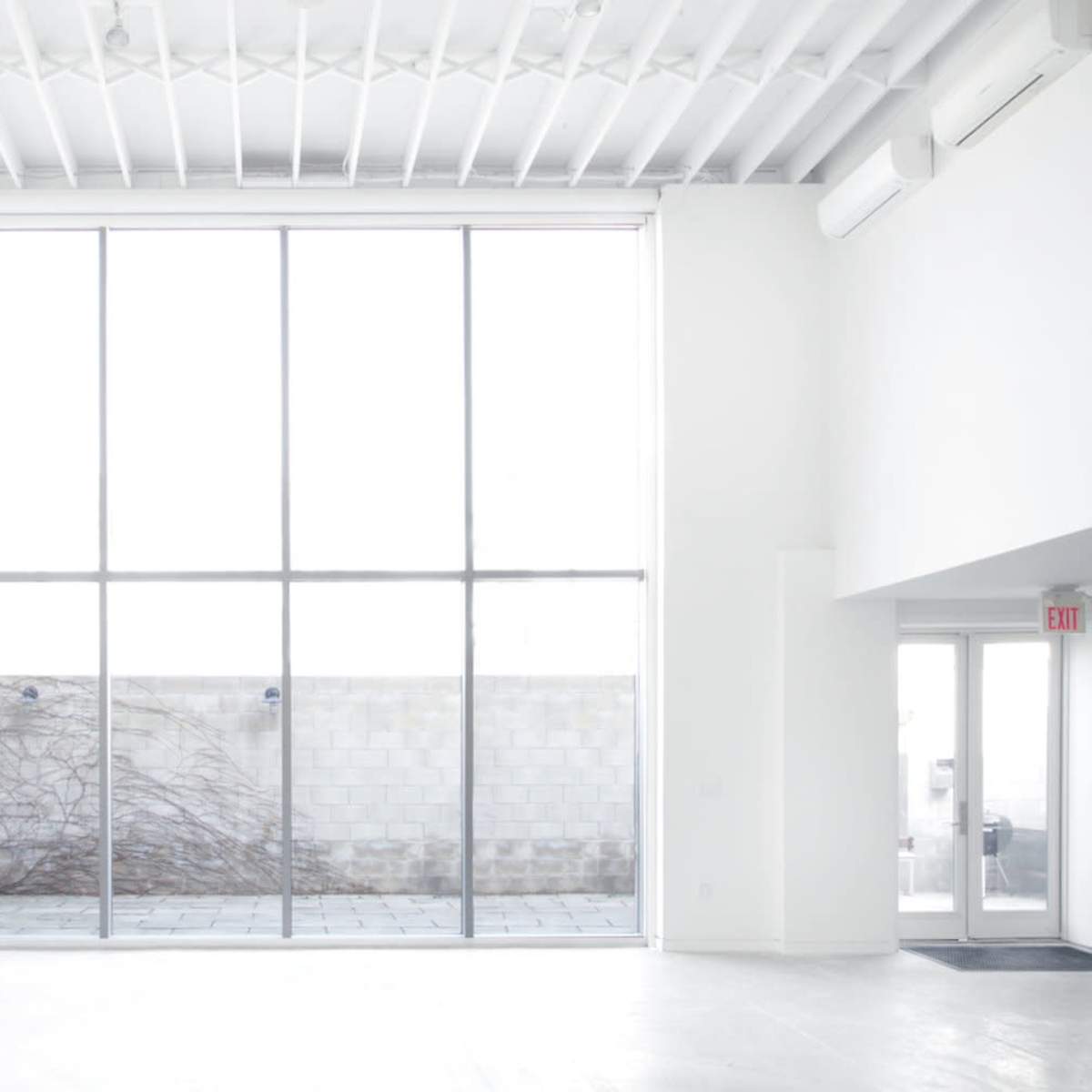 A minimalist interior with large glass windows overlooking a bare outdoor space.