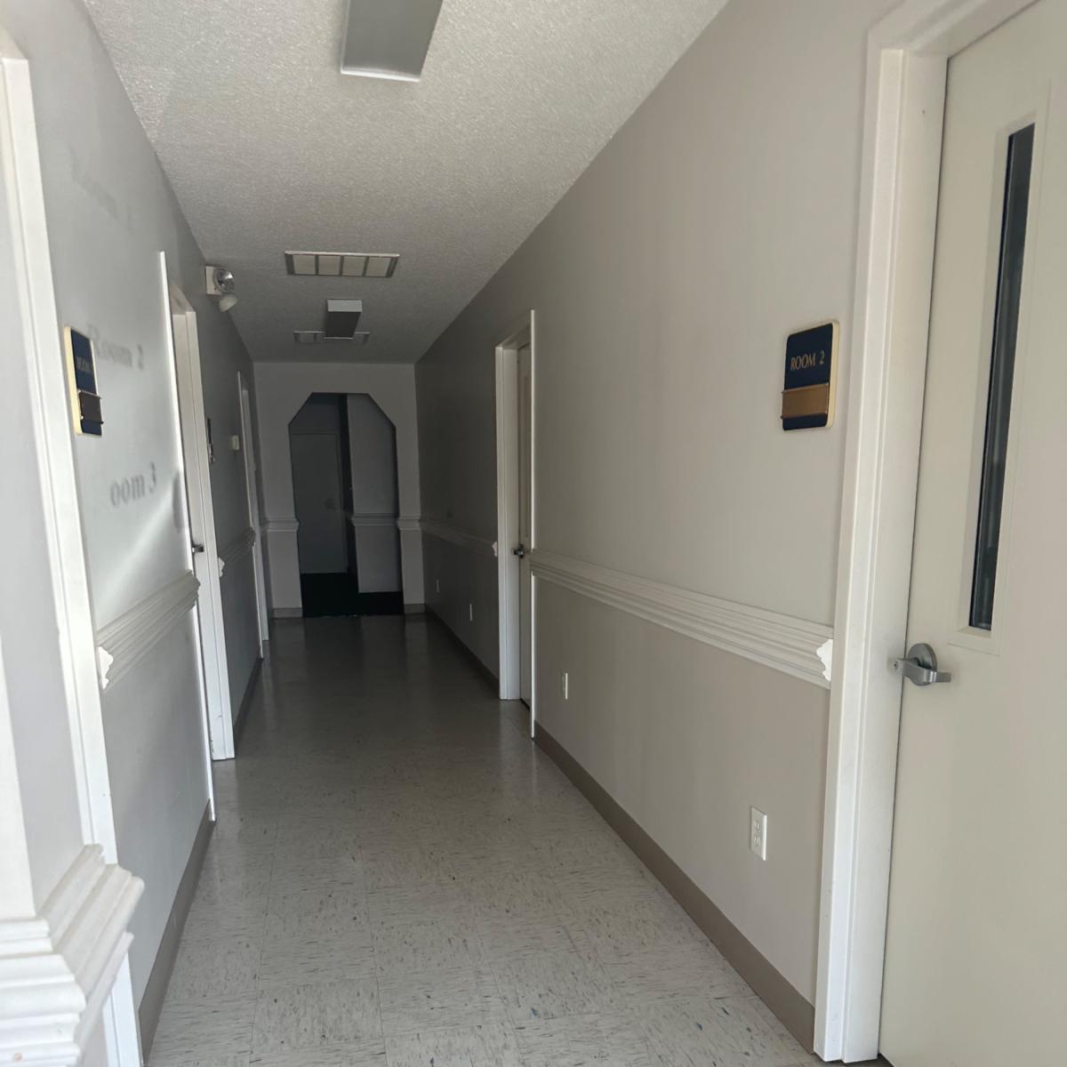 A long, narrow hallway with closed doors on either side and a doorway at the far end.
