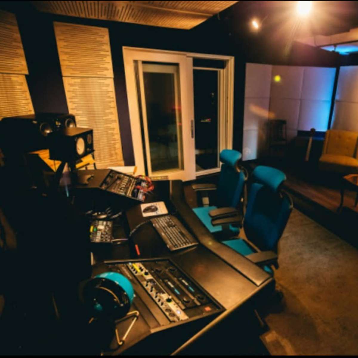A recording studio with a control desk, two blue chairs, and a seating area featuring a sofa and a chair.