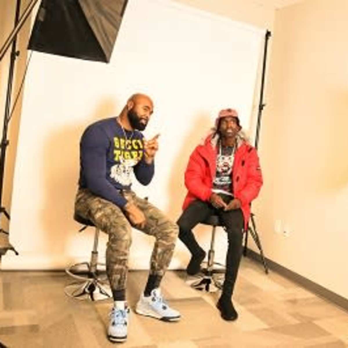Two men sit on stools in a photography studio, surrounded by lighting equipment and a neutral backdrop.