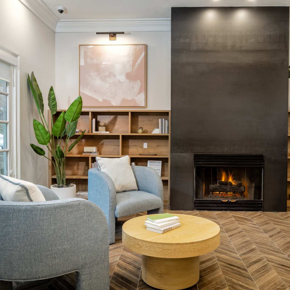 A cozy interior space featuring two light blue armchairs, a round wooden coffee table, and a modern fireplace surrounded by wooden shelving.