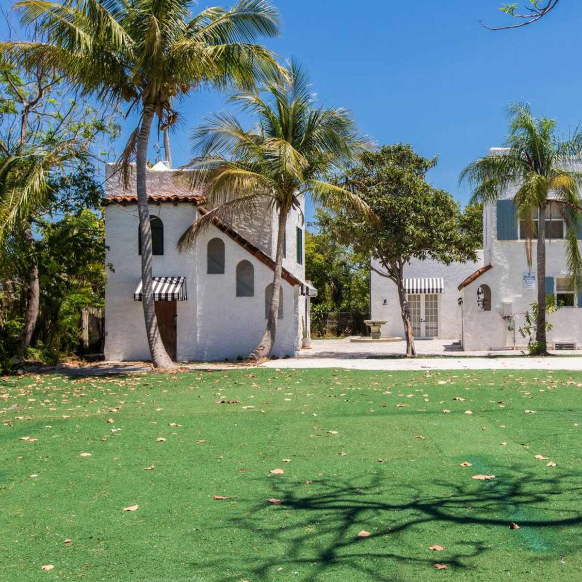Two white stucco buildings surrounded by palm trees and a green lawn under a clear blue sky.