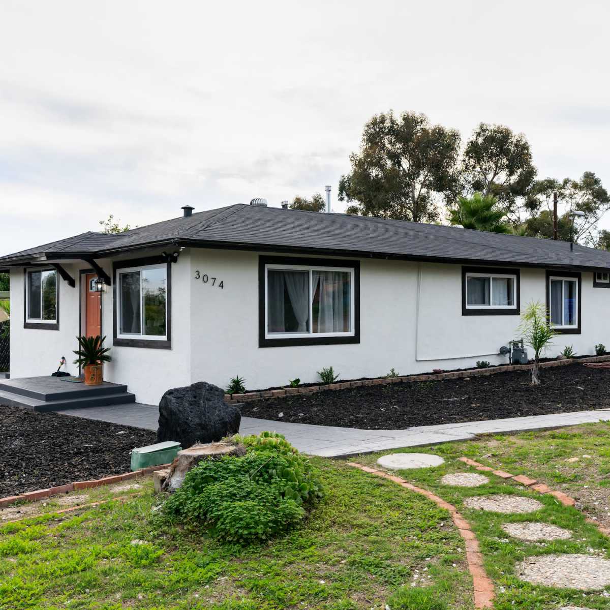 A single-story, modern white house with a black roof and landscaped yard is shown in the image.