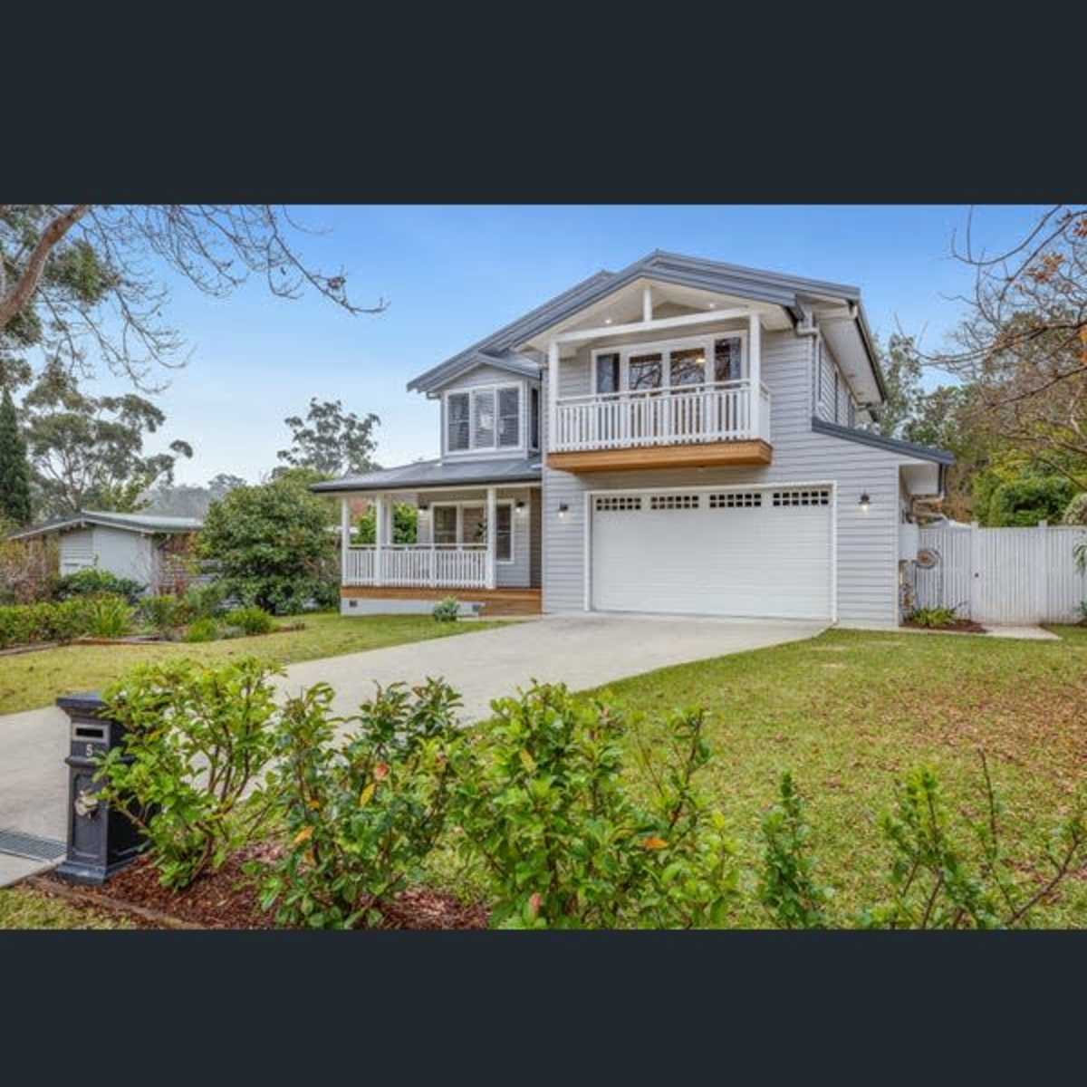 A two-story, light-colored house with a front porch and a garage sits in a landscaped yard.
