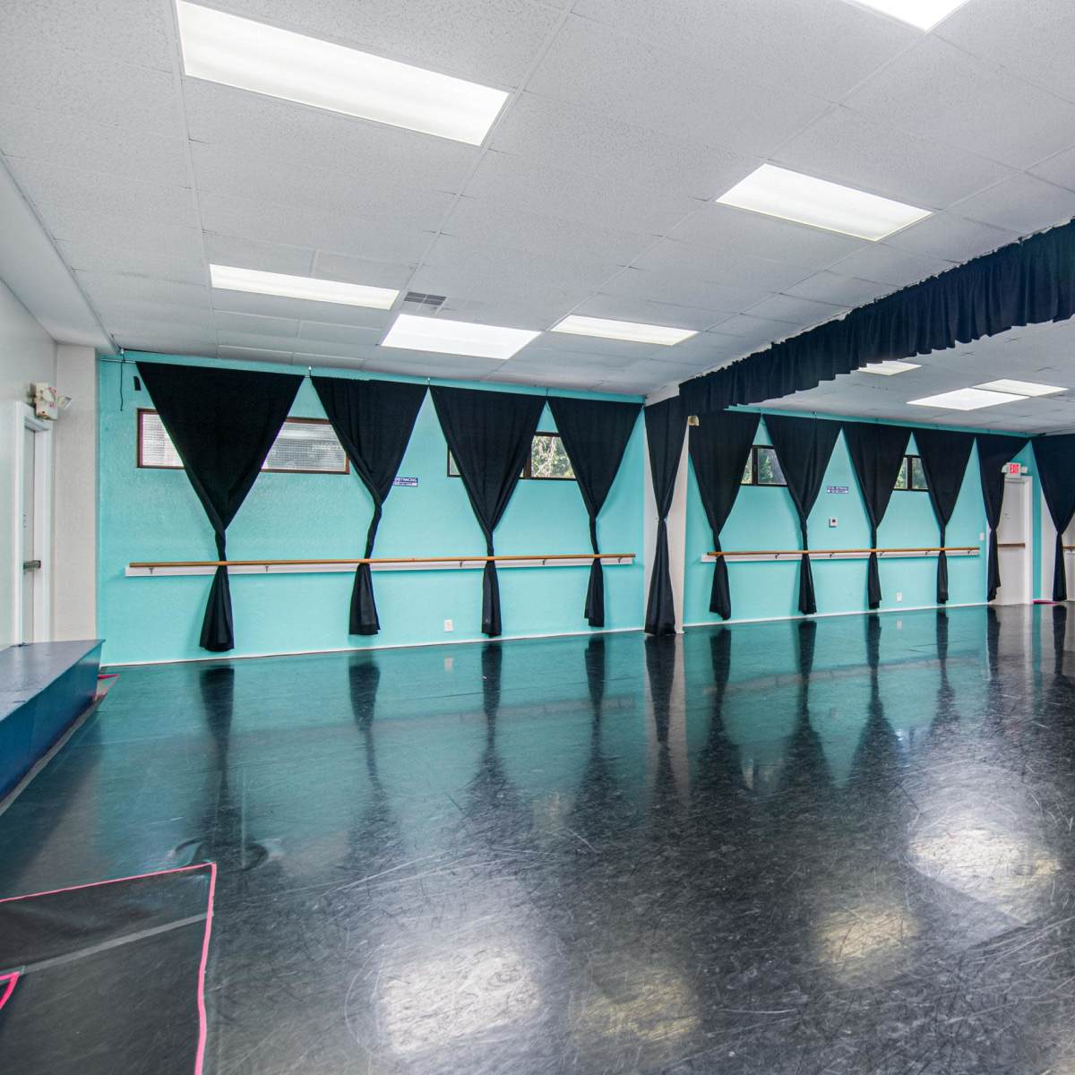 A spacious dance studio with a black floor, mirrored walls, and black curtains along one side.